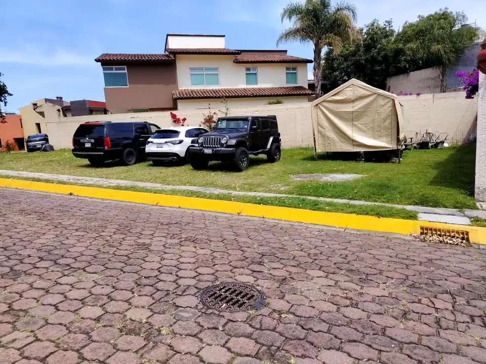 El frente largo del terreno, con pasto parejo y la casa vecina al fondo